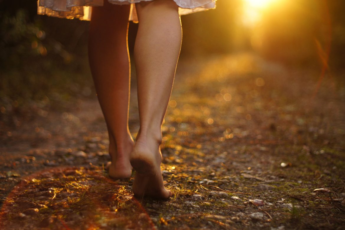 Woman walks barefoot along a forest path into the sunrise
